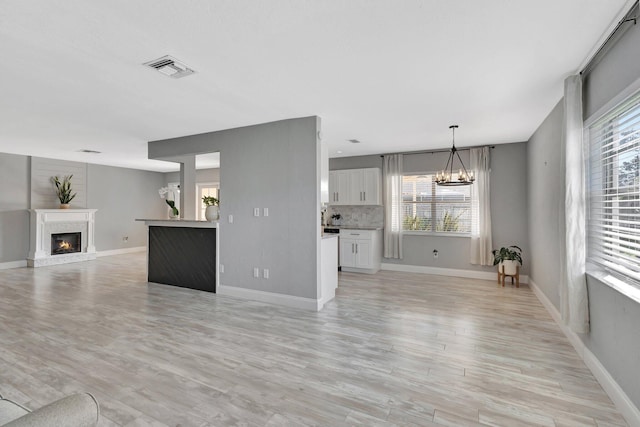 1181 Larch Way, Wellington, FL 33414 - unfurnished living room featuring a chandelier, healthy amount of natural light, a glass covered fireplace, and light wood-style floors