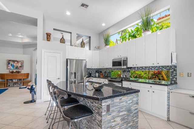 kitchen with stainless steel appliances, a sink, light tile patterned flooring, backsplash, and a kitchen bar