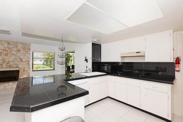 1117 SE Mendoza Ave, Port Saint Lucie, FL 34952 - kitchen with under cabinet range hood, a sink, dark countertops, and a peninsula