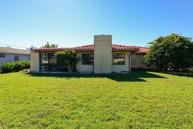 1117 SE Mendoza Ave, Port Saint Lucie, FL 34952 - rear view of property with a chimney, a lawn, a tiled roof, and stucco siding