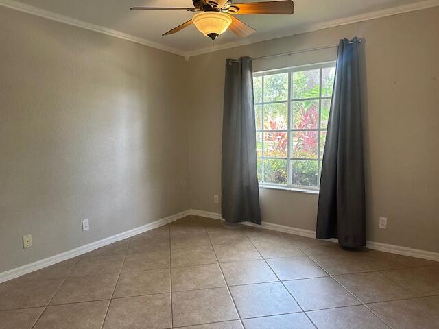 unfurnished room featuring a ceiling fan, plenty of natural light, tile patterned floors, crown molding, and baseboards