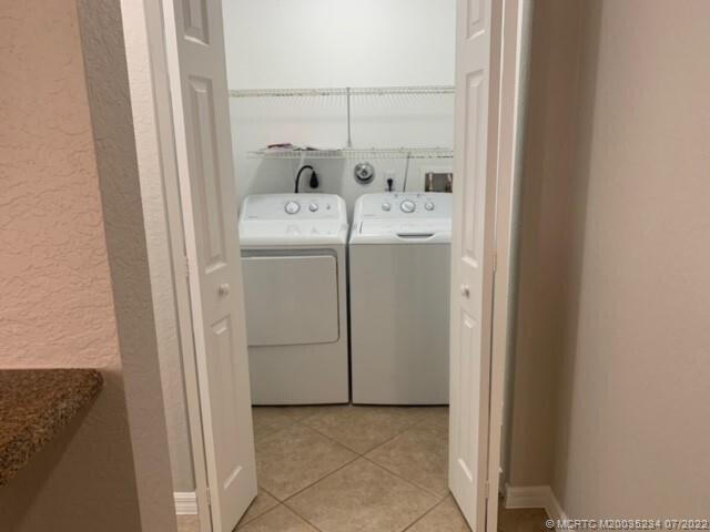 washroom with washing machine and clothes dryer, light tile patterned floors, and a textured wall