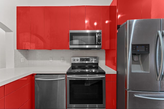 kitchen with stainless steel appliances, red cabinetry, backsplash, and light countertops