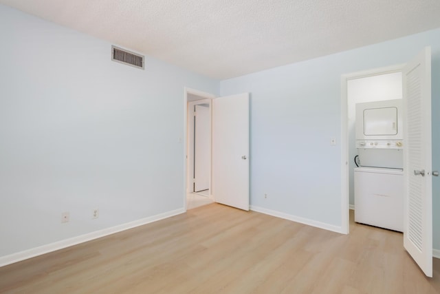 4411 Trevi Ct Unit 303, Lake Worth, FL 33467 - unfurnished bedroom featuring stacked washer and clothes dryer, light wood-type flooring, baseboards, and a textured ceiling