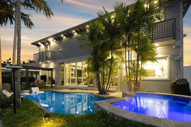 311 SE 11th St, Pompano Beach, FL 33060 - back of house at dusk featuring a balcony, an outdoor pool, an outdoor hot tub, and a patio