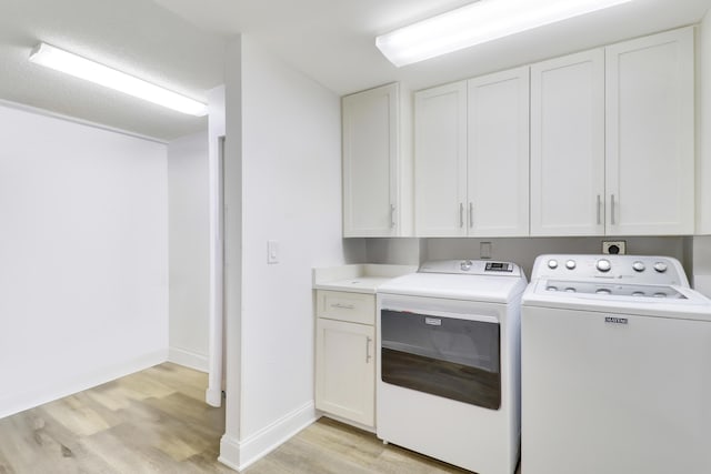 clothes washing area with separate washer and dryer, light wood-style flooring, cabinet space, and baseboards