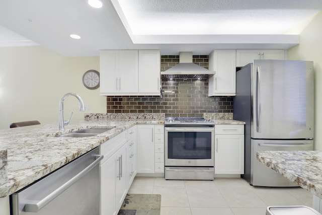 kitchen with appliances with stainless steel finishes, wall chimney range hood, a sink, light tile patterned floors, and decorative backsplash