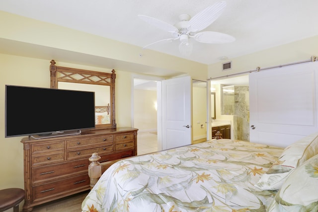 bedroom with ensuite bathroom, tile patterned flooring, a ceiling fan, and a barn door