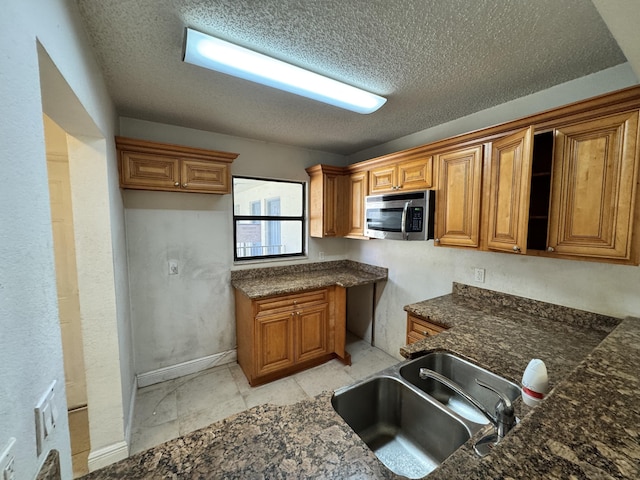 1453 Lake Crystal Dr Unit H, West Palm Beach, FL 33411 - kitchen featuring stainless steel microwave, a sink, brown cabinets, a textured ceiling, and dark stone countertops