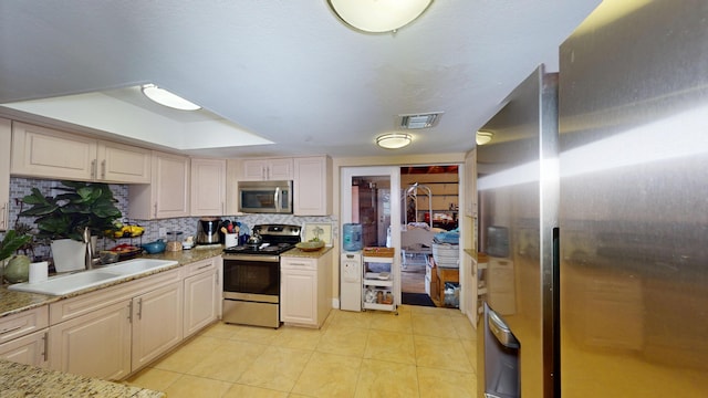 kitchen with stainless steel appliances, light tile patterned floors, tasteful backsplash, a sink, and light stone counters