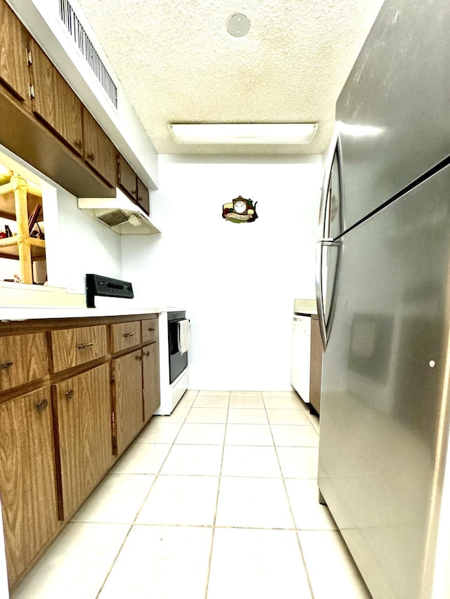 kitchen featuring white appliances, under cabinet range hood, light countertops, light tile patterned floors, and a textured ceiling