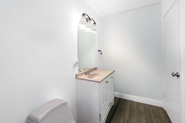 half bathroom with wood finished floors, vanity, toilet, and baseboards