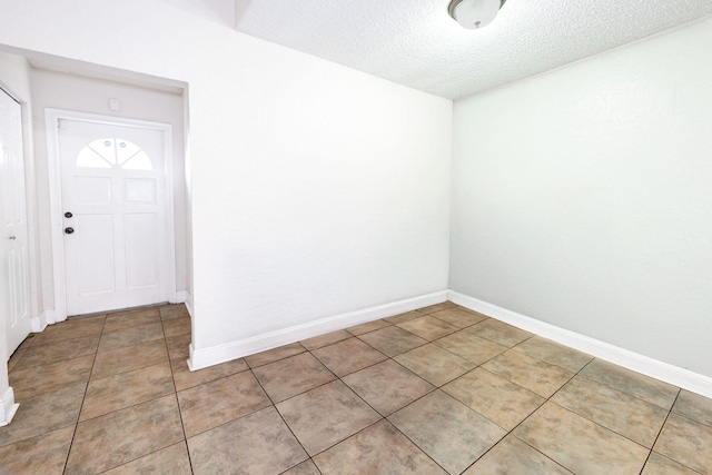 foyer entrance featuring a textured ceiling, light tile patterned floors, and baseboards