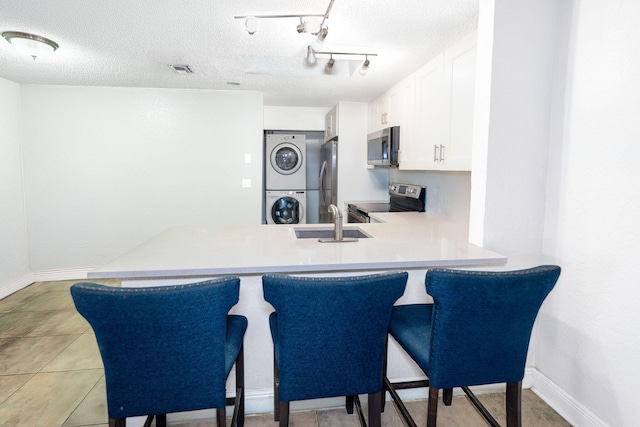 kitchen with stacked washer / dryer, stainless steel appliances, a sink, white cabinetry, and light countertops