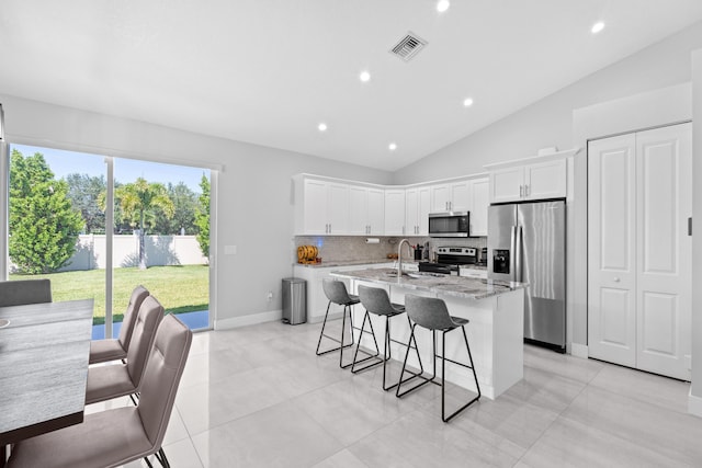 12111 Sugar Pine Trl, Wellington, FL 33414 - kitchen with stainless steel appliances, a kitchen island with sink, decorative backsplash, lofted ceiling, and light stone counters