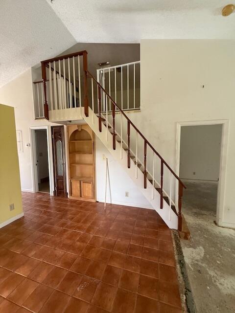 stairs with high vaulted ceiling, tile patterned floors, a textured ceiling, and baseboards