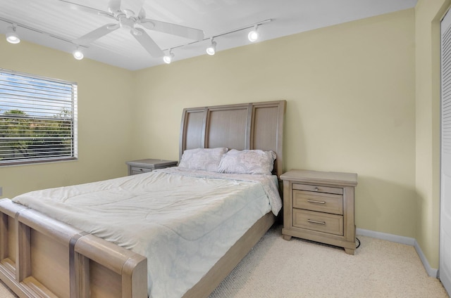 bedroom featuring rail lighting, light colored carpet, baseboards, and ceiling fan