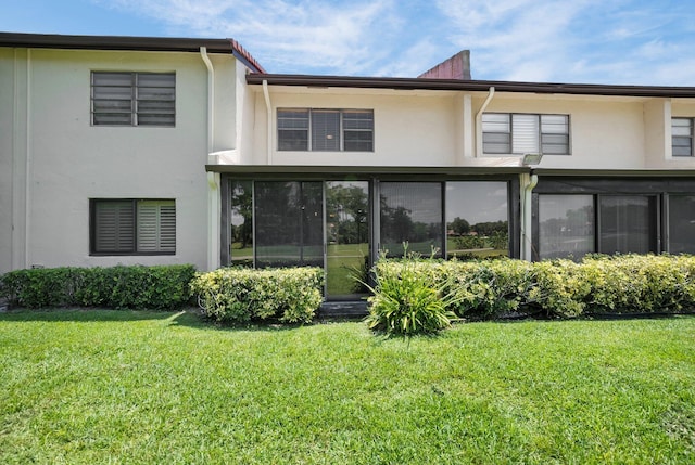 rear view of house with stucco siding, a lawn, and a sunroom