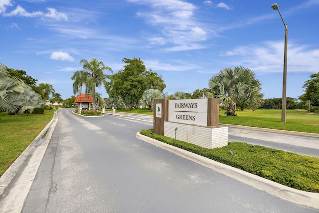 view of asphalt road featuring street lighting, curbs, and a gated entry