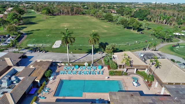 aerial view of property and surrounding area with a pool, a golf club, and a tree filled landscape