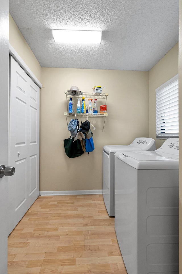 clothes washing area featuring washer and clothes dryer, light wood-style floors, a textured ceiling, and baseboards