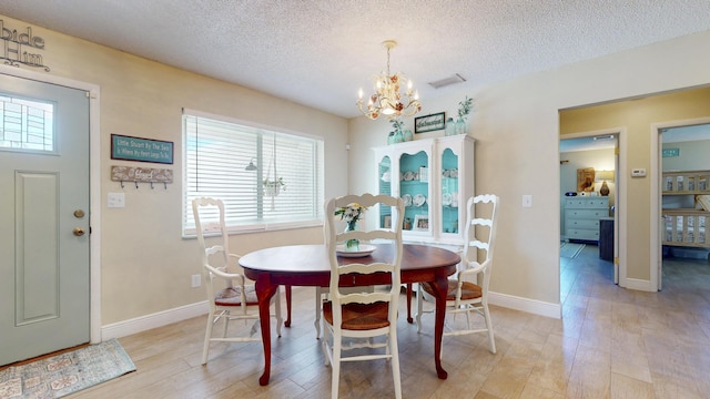 dining room featuring healthy amount of natural light, a chandelier, light wood-style flooring, and a textured ceiling