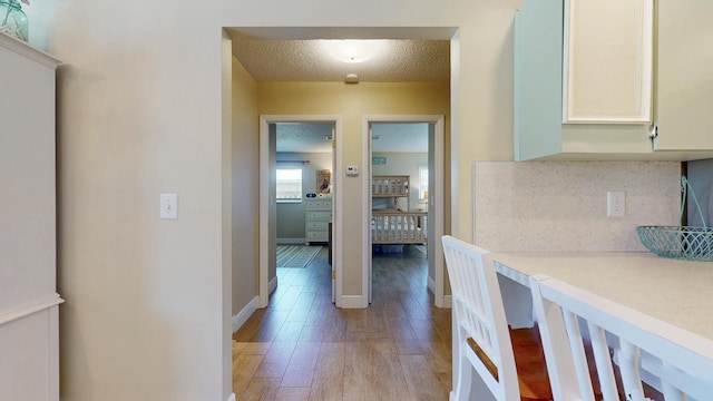 hall featuring light wood finished floors, a textured ceiling, and baseboards