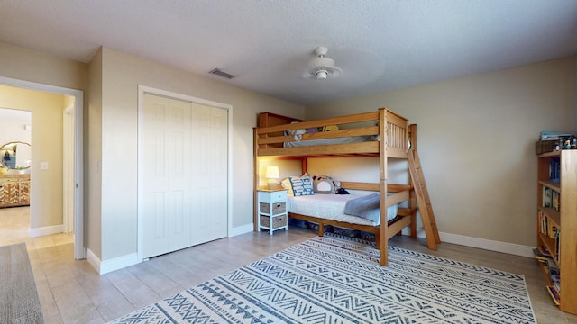 bedroom featuring light wood-style flooring, baseboards, a textured ceiling, and a closet