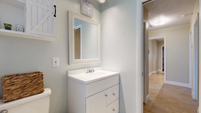 bathroom with toilet, wood finished floors, baseboards, vanity, and a textured ceiling