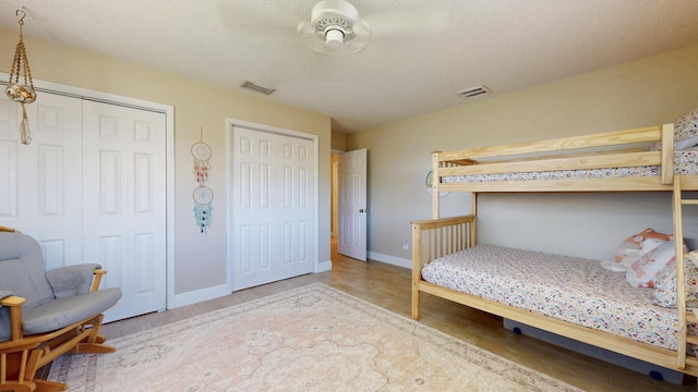bedroom with multiple closets, wood finished floors, baseboards, and a textured ceiling