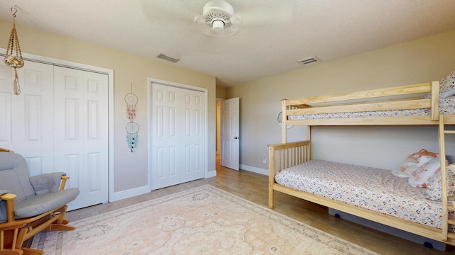 bedroom with two closets, wood finished floors, baseboards, a textured ceiling, and a ceiling fan