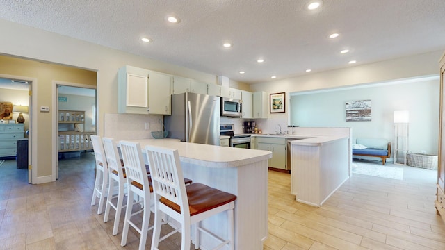 kitchen with stainless steel appliances, a peninsula, light wood-type flooring, light countertops, and a kitchen bar
