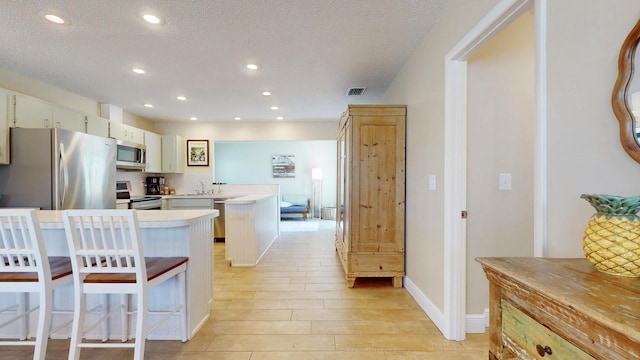 kitchen featuring appliances with stainless steel finishes, a peninsula, light wood-type flooring, a kitchen bar, and light countertops