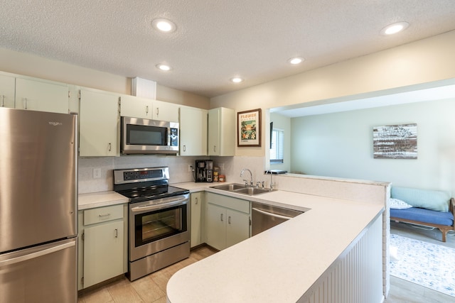 kitchen with appliances with stainless steel finishes, a sink, light countertops, decorative backsplash, and a peninsula