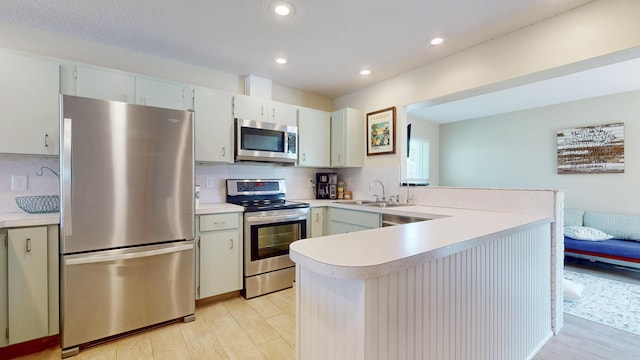 kitchen featuring stainless steel appliances, a peninsula, light countertops, light wood finished floors, and recessed lighting