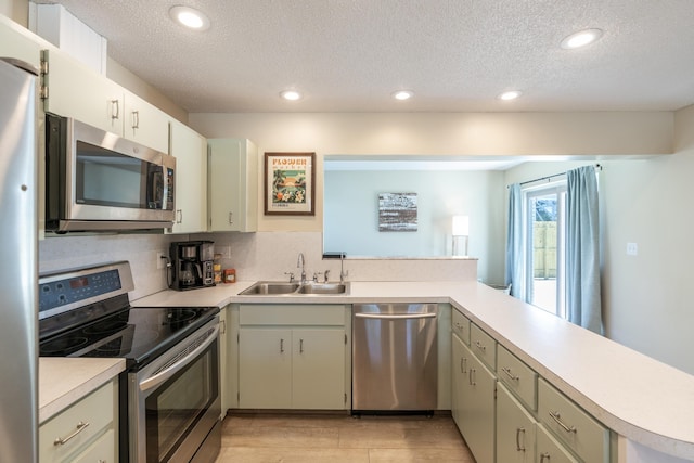 kitchen with stainless steel appliances, a sink, a peninsula, a textured ceiling, and light countertops