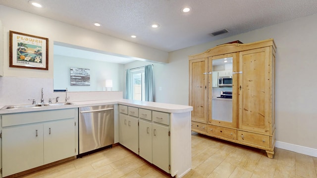 kitchen featuring stainless steel appliances, a sink, a peninsula, light countertops, and a textured ceiling