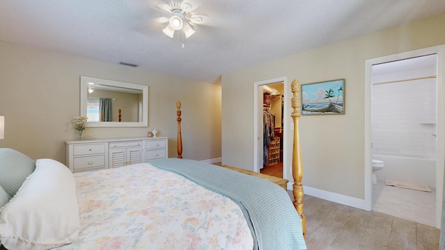 bedroom featuring light wood-style flooring, a walk in closet, baseboards, ceiling fan, and connected bathroom