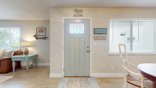 entryway with healthy amount of natural light, baseboards, light wood-type flooring, and a textured ceiling