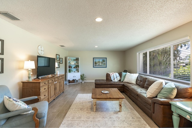 living room featuring a textured ceiling, light wood-type flooring, recessed lighting, and baseboards