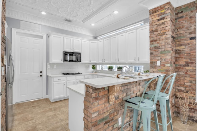 1909 Flower Dr, Palm Beach Gardens, FL 33410 - kitchen with black microwave, a kitchen bar, a peninsula, light countertops, and white cabinets