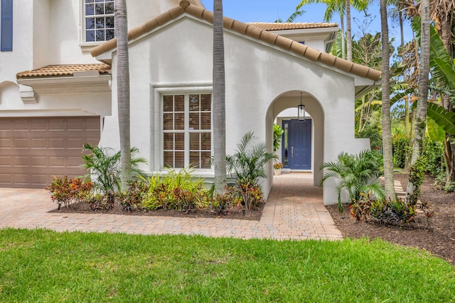 1909 Flower Dr, Palm Beach Gardens, FL 33410 - view of exterior entry with a tiled roof, an attached garage, and stucco siding