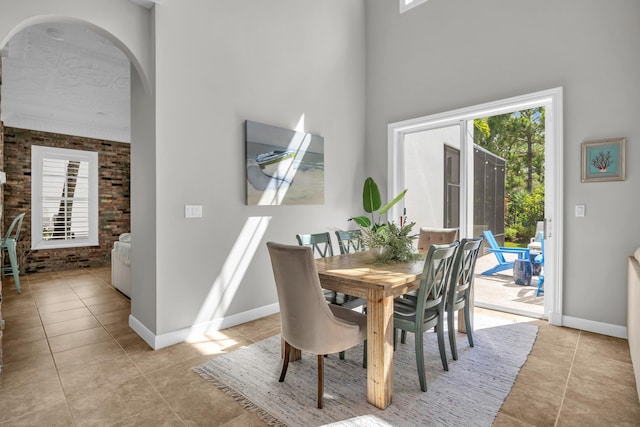 1909 Flower Dr, Palm Beach Gardens, FL 33410 - dining room featuring brick wall, light tile patterned floors, arched walkways, and a high ceiling