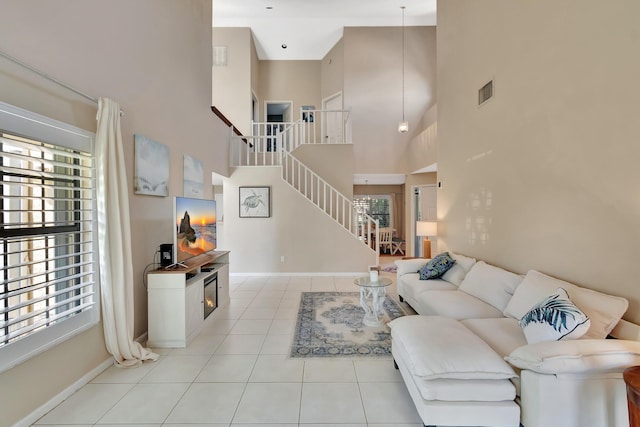 living room with a towering ceiling, stairway, light tile patterned flooring, and baseboards