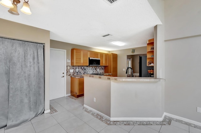 kitchen with black microwave, a sink, backsplash, light tile patterned floors, and baseboards