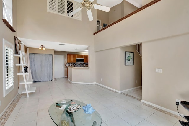 unfurnished living room with a towering ceiling, light tile patterned flooring, baseboards, and a ceiling fan