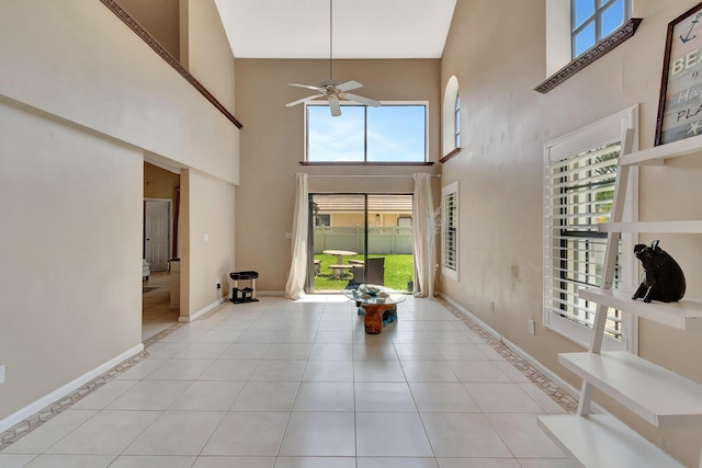 tiled entrance foyer with a towering ceiling, a ceiling fan, and baseboards