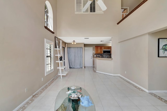 unfurnished living room featuring healthy amount of natural light, a towering ceiling, baseboards, and light tile patterned floors