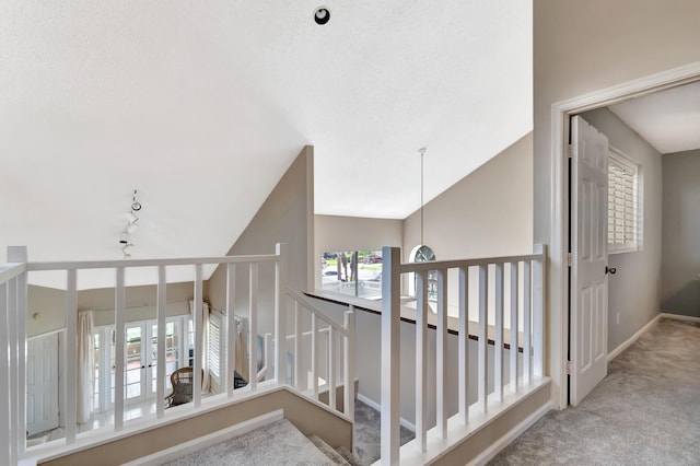 hallway with carpet floors, rail lighting, baseboards, and lofted ceiling