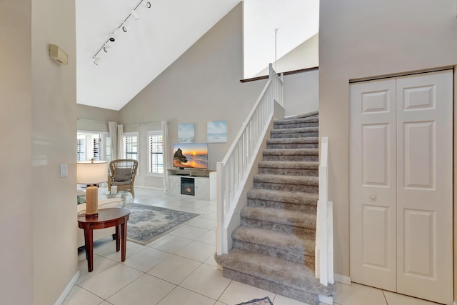 stairway with high vaulted ceiling, track lighting, tile patterned flooring, and baseboards